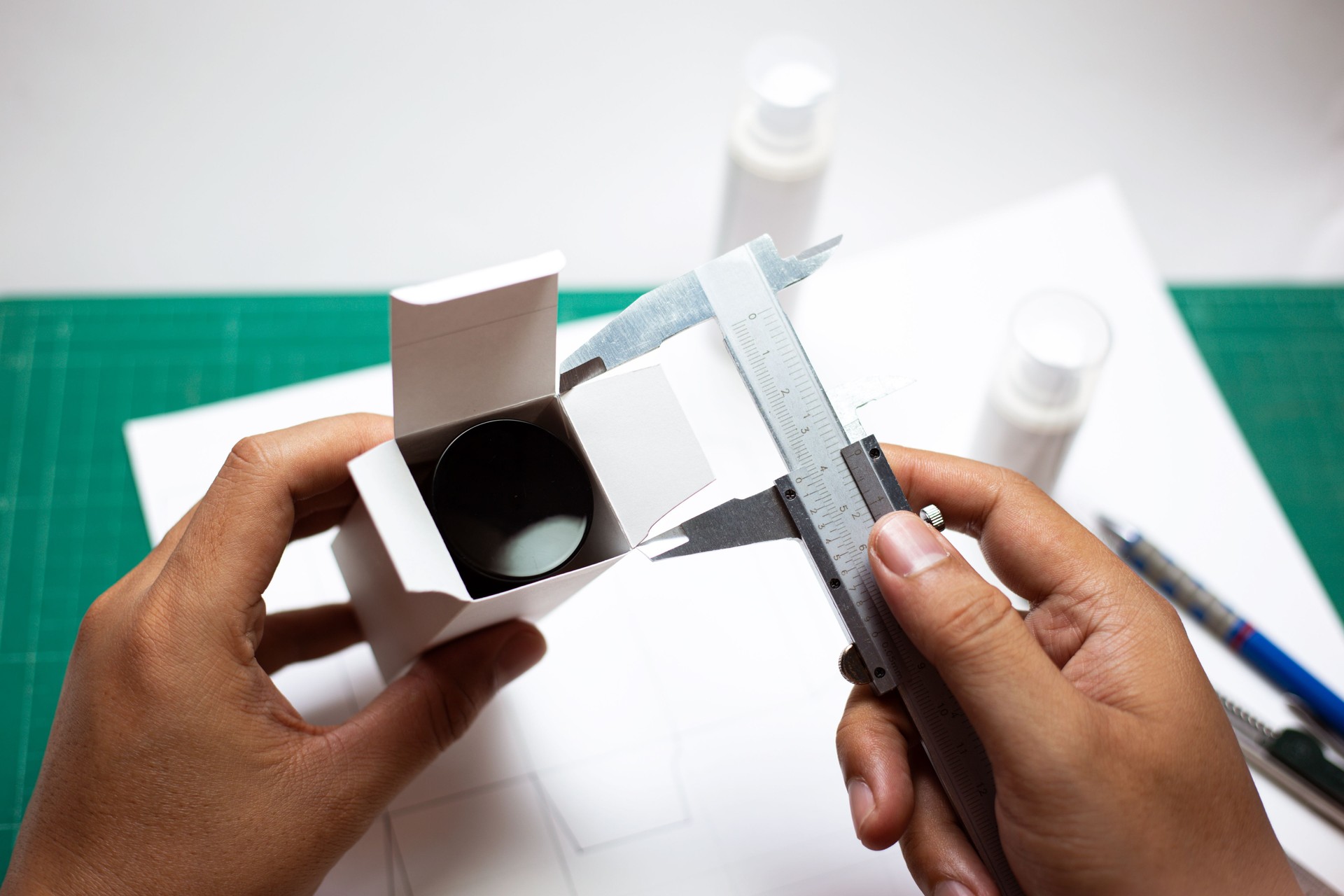 Hand holding vernier caliper to measure the size of the cosmetics container.